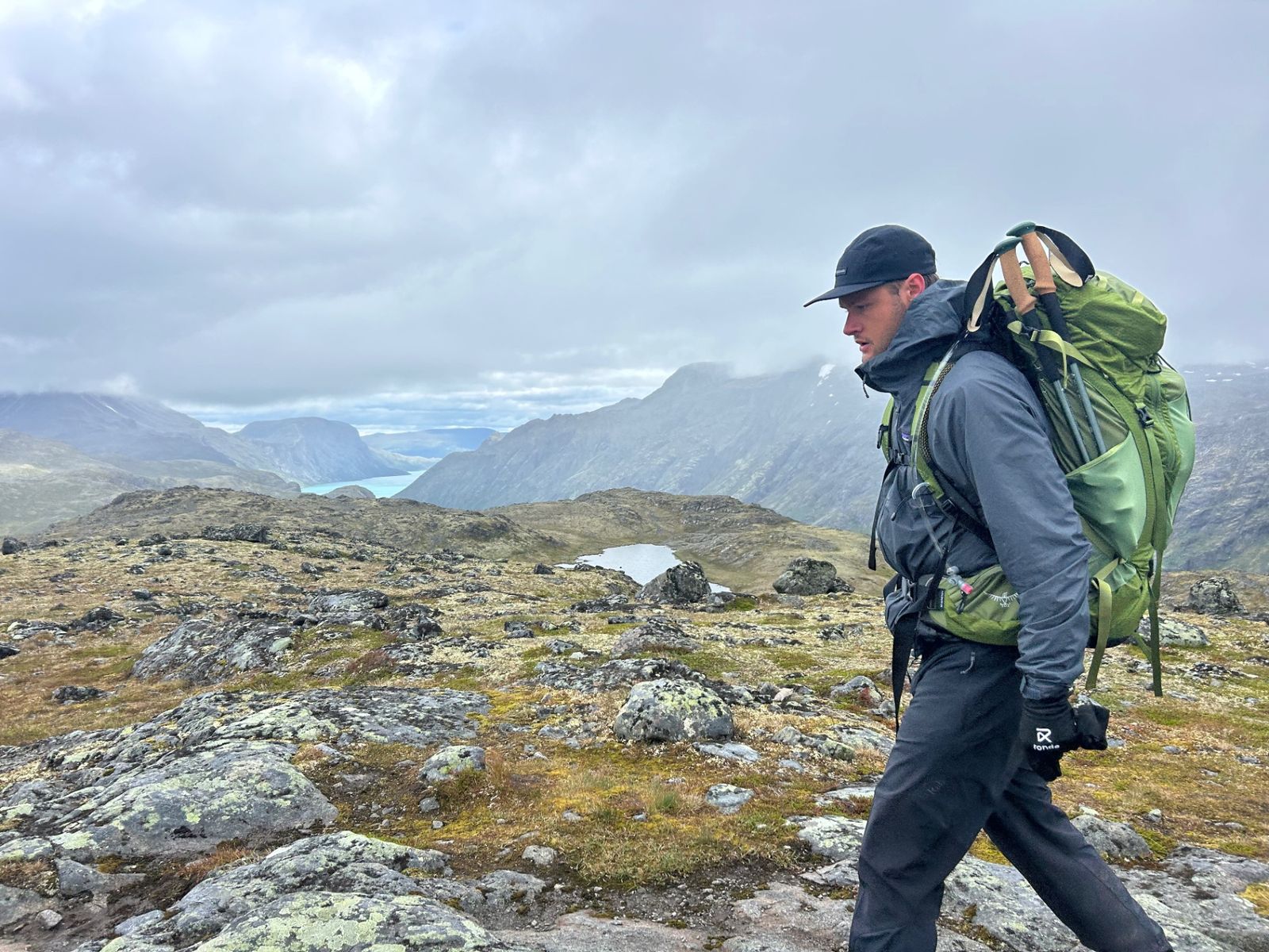 Trekker with a fully loaded Osprey pack on a trail above the fjord