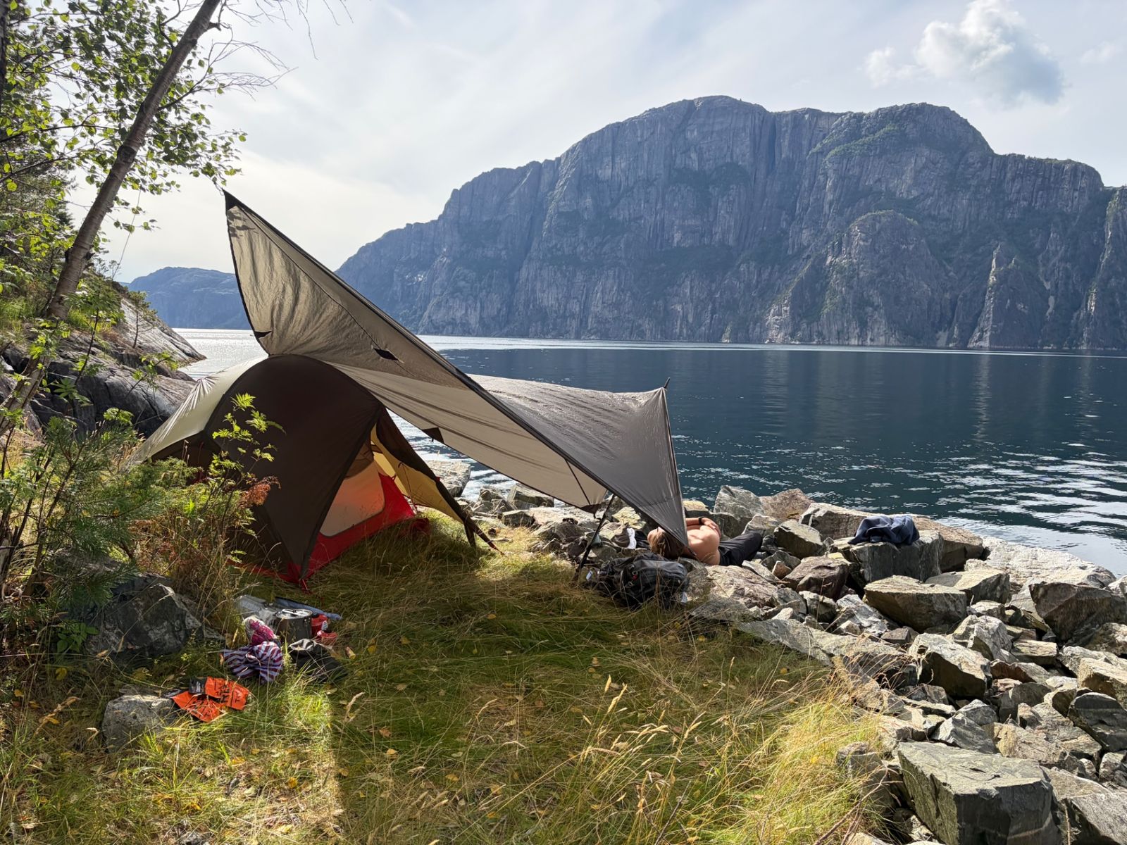 Stoic tarp and MSR tent pitched at Lysefjord, someone resting on the rocks by the water